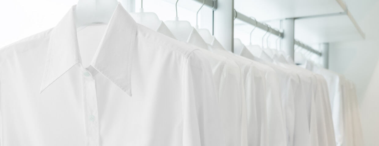 multiple white button up shirts hanging on racks