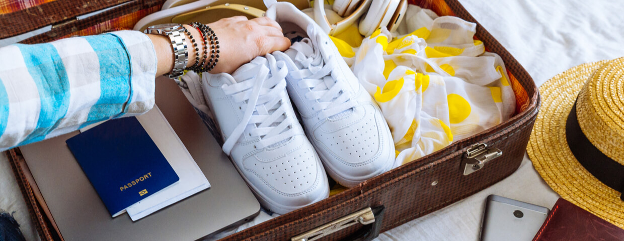 closeup of woman's suitcase open, packing concept, woman putting white sneakers into suitcase