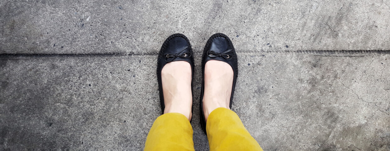 top view, selfie of woman's feet wearing mustard-yellow trouser and black shoe standing on a concrete floor