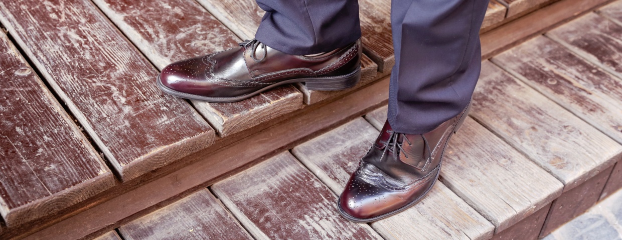 dress shoes concept, closeup of burgundy cap toe dress shoe and navy suit, man standing on wooden stairs