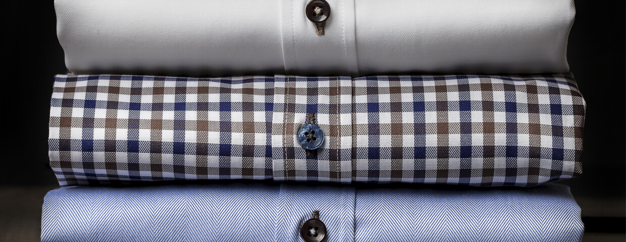 closeup stack of folded mens dress shirts, solid white, plaid, solid blue