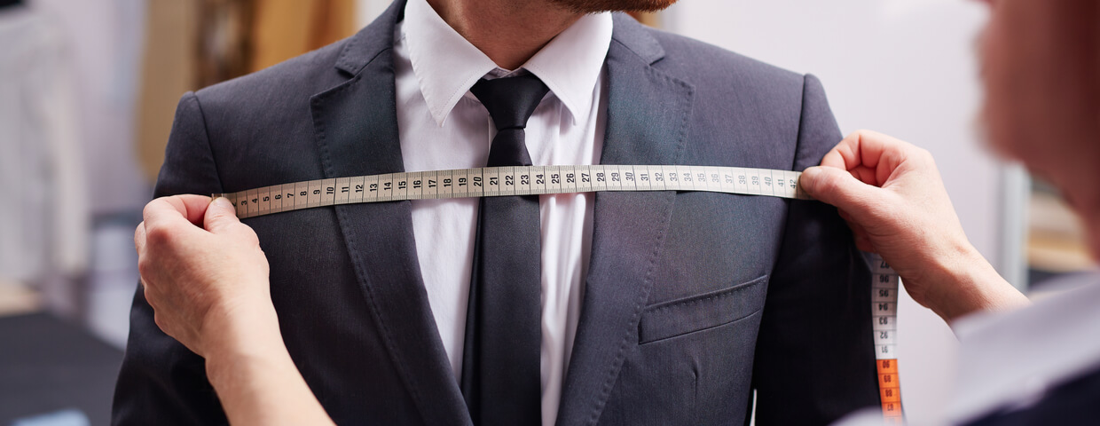 Mid section portrait of tailor fitting suit, measuring width of man who is wearing suit
