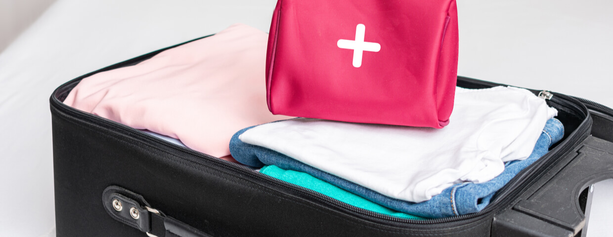 Open suitcase packed with clothes and a first aid kit set on top