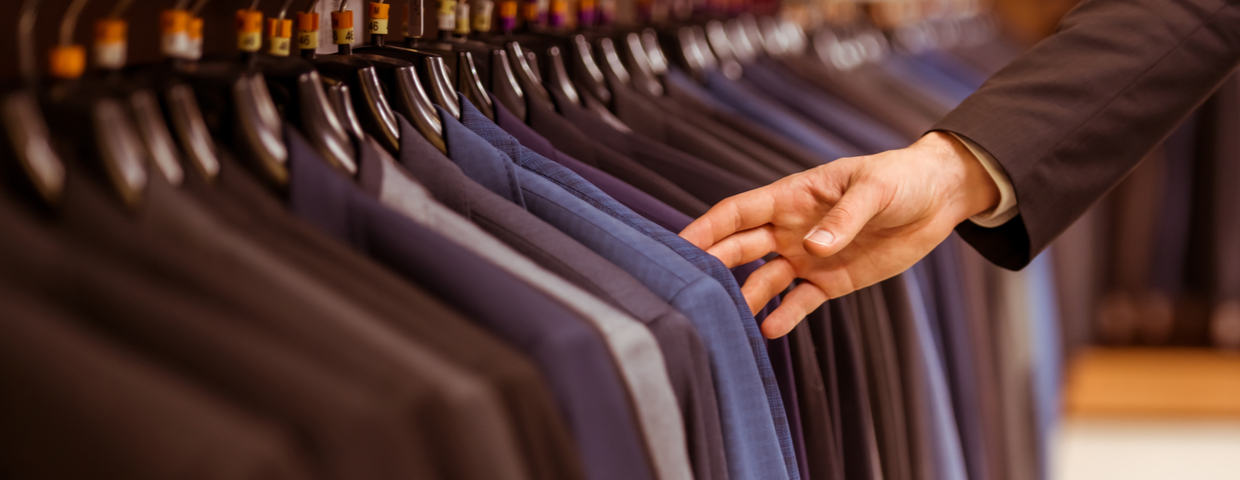 multiple mens suits hung up on clothing rack, shopping concept, with a hand choosing one suit