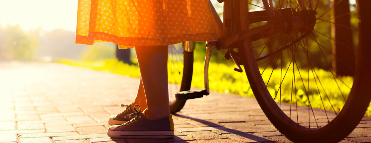 Girls legs and long vintage orange skirt next to bike in the sun