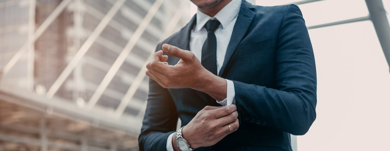 man in suit adjusting button on shirt sleeve