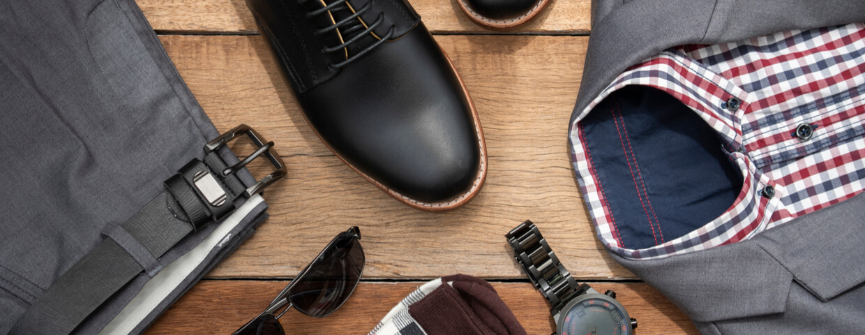 Creative fashion design for men, clothing set and accessories on wooden background include black derby shoes, gray suit, pants, belt, sunglass, sock and plaid shirt. Flat lay, top view