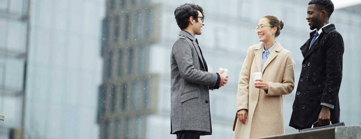 Multi-ethnic group of smiling business people meeting in snowy city street, smiling and talking. Winter clothing concept